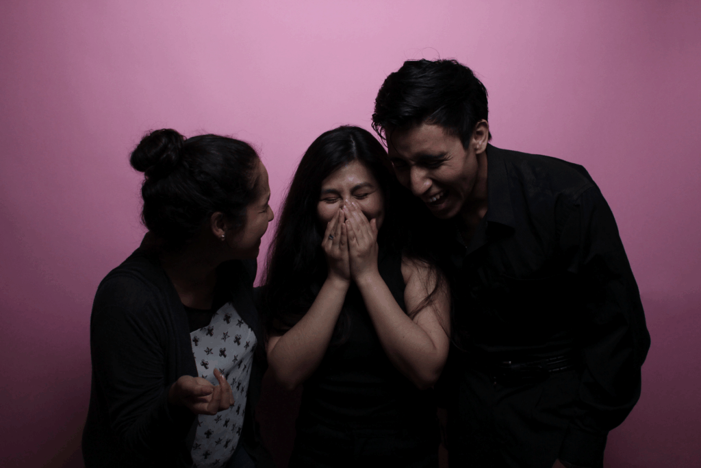 Three friends share a joyful moment with laughter against a pink backdrop.