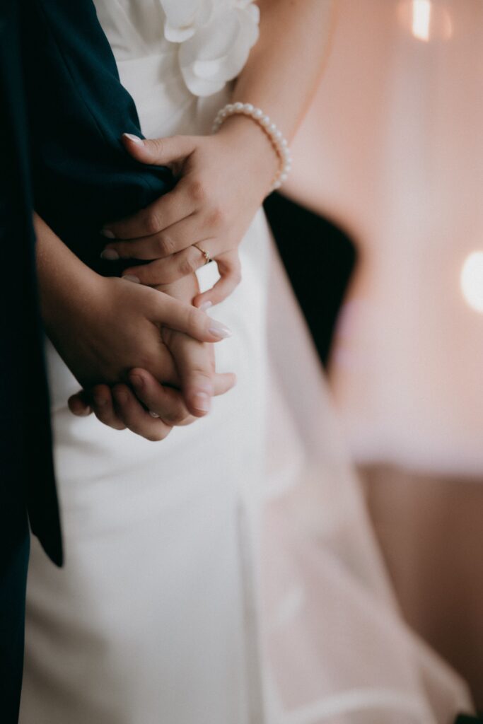 Tender close-up photo of bride and groom holding hands, symbolizing love and unity.