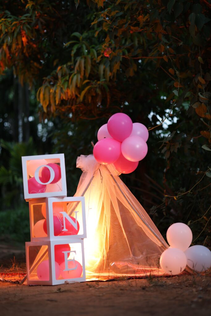 Vibrant pink balloon and block decoration for a baby's first birthday set outdoors.